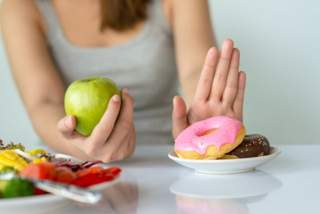 Woman holding a green apple, saying no to junk food doughnuts on a plate
