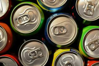 Top-down view of multiple soft drink cans arranged closely together, showing the tops of the cans with pull tabs. 