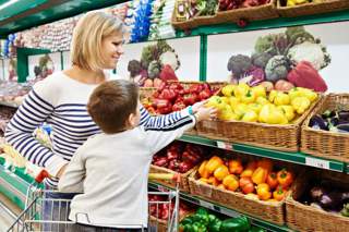 Mum, toddler son in fresh food section of supermarket selecting a capsicum