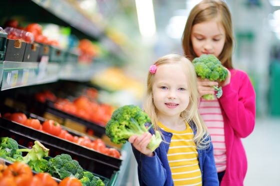 Sisters holding broccoli in the supermarket fresh food aisle