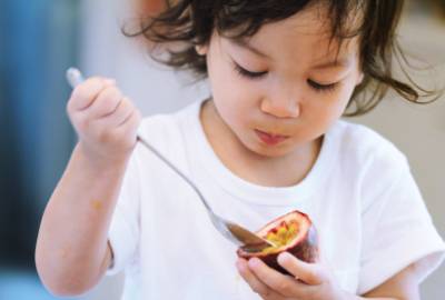 Toddler eating passionfruit with a spoon